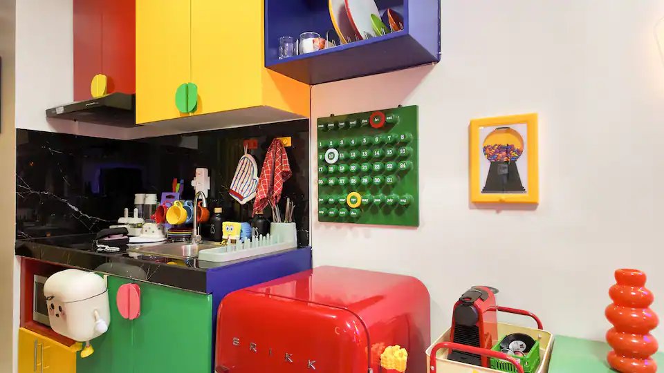 Kitchenette wide shot with color-block cabinets, candy-red fridge and yellow framed art