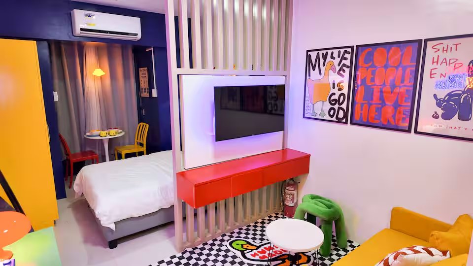 Living room TV in front of confetti wall art with yellow cabinet and Memphis posters