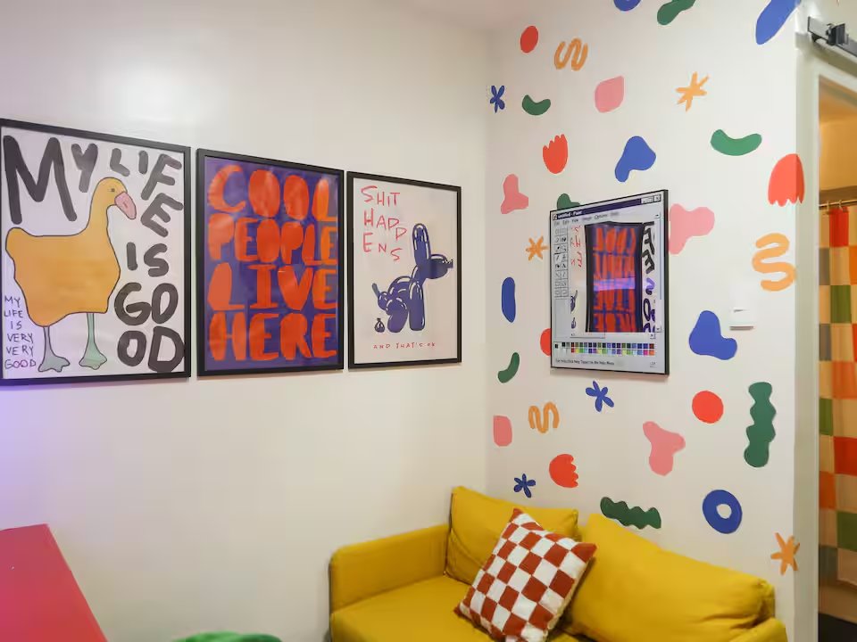Yellow sofa with checker pillow against confetti art wall reading My Life Is Good and Live Here